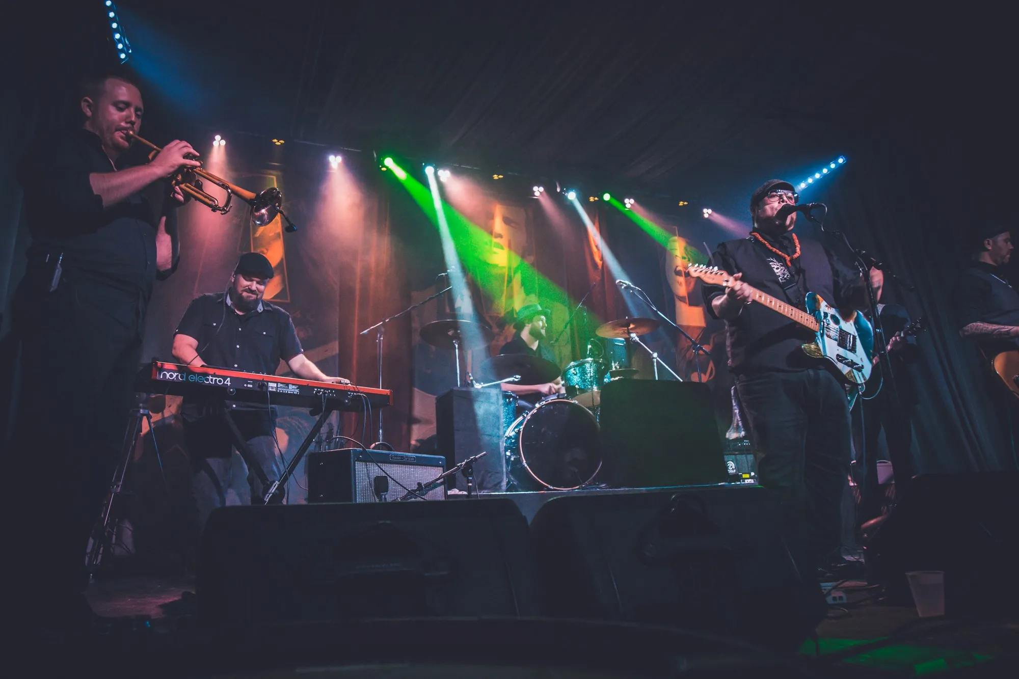 Full band on a lit stage with horns, keys at the left.